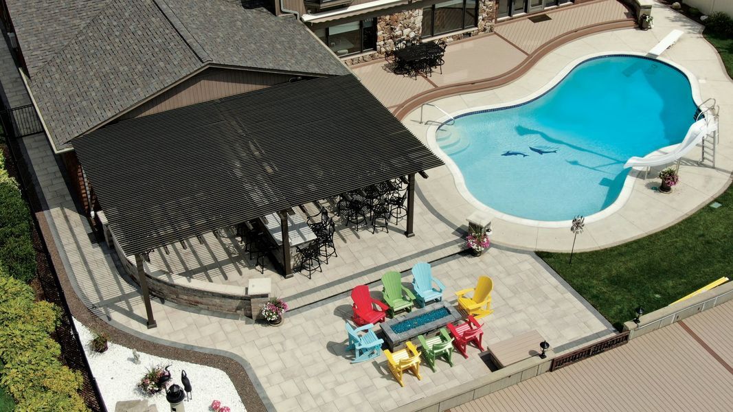 Aerial view of a backyard with a pool, patio, pergola, and colorful Adirondack chairs.