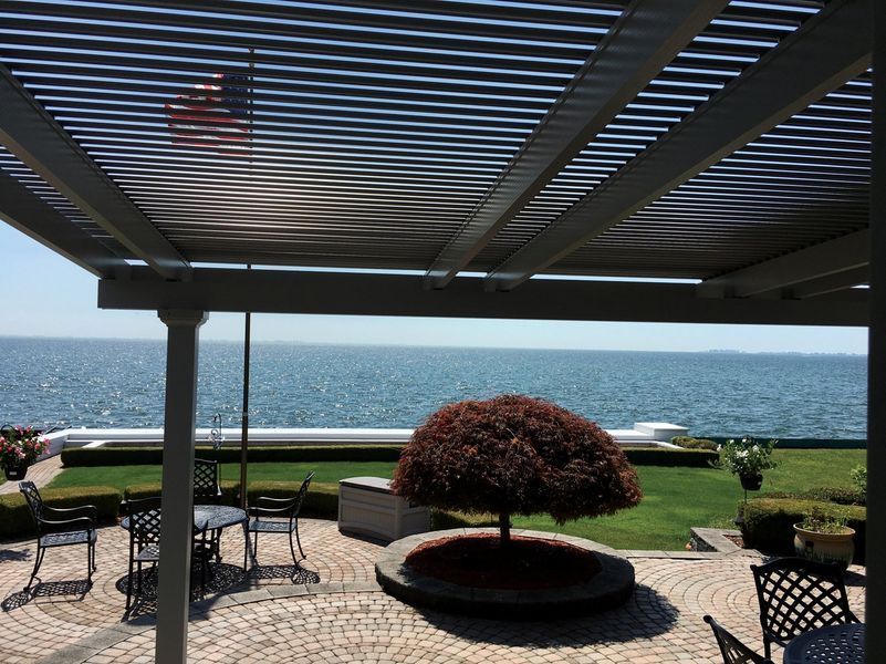 Patio with view of ocean; pergola overhead, small tree in garden.