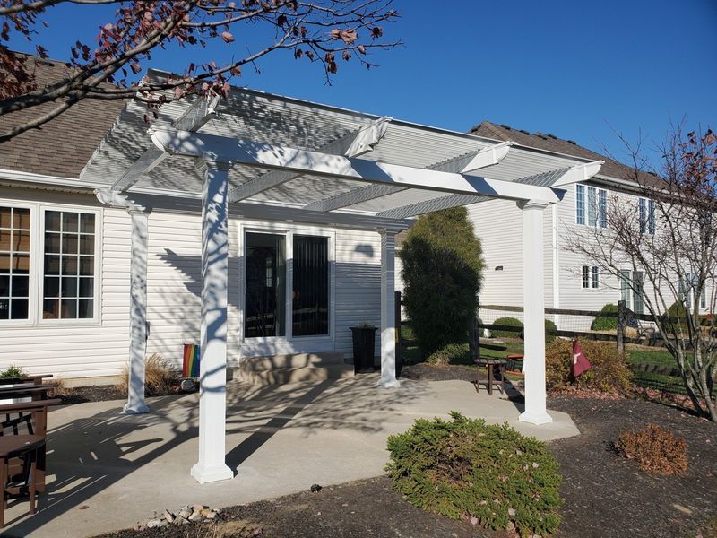 White pergola over a concrete patio outside a house with a clear blue sky.