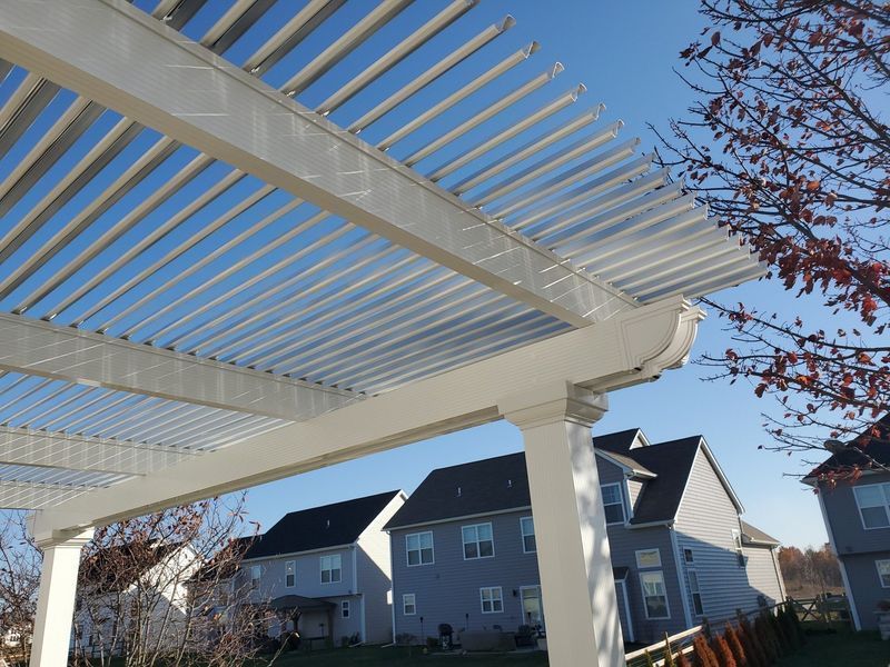 White pergola with angled slats, blue sky background, overlooking houses.