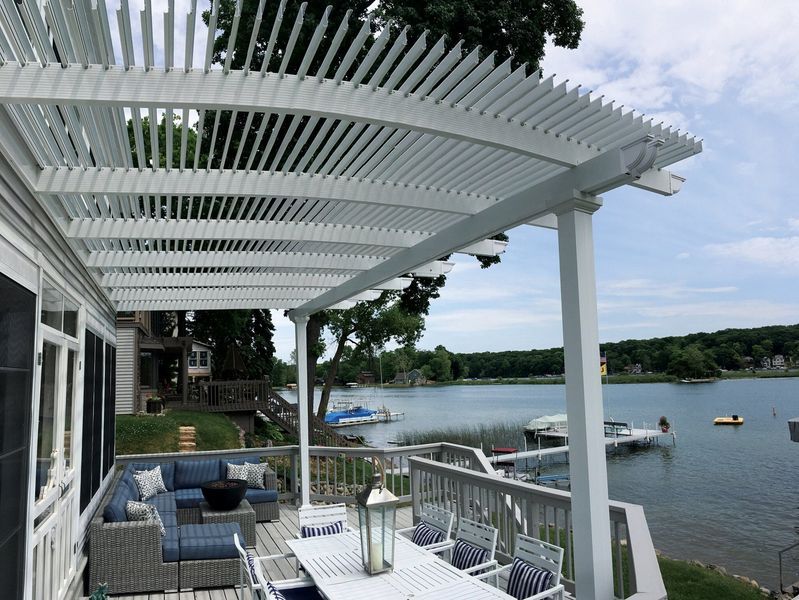 White pergola over a deck overlooking a lake, with furniture and boats.