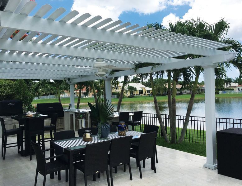 White pergola over outdoor dining area, black furniture, and lake view.
