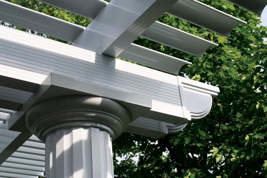 Close-up of a white pergola with fluted column and horizontal slats, against a green leafy backdrop.