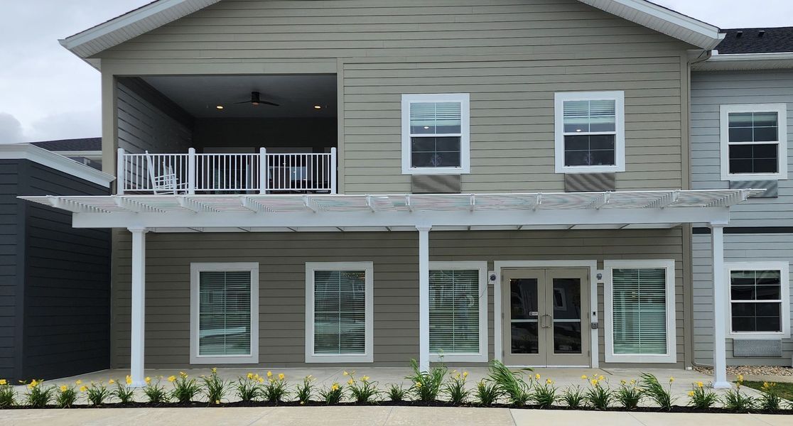 Beige and gray building with a pergola-covered patio, windows, and an upper balcony.