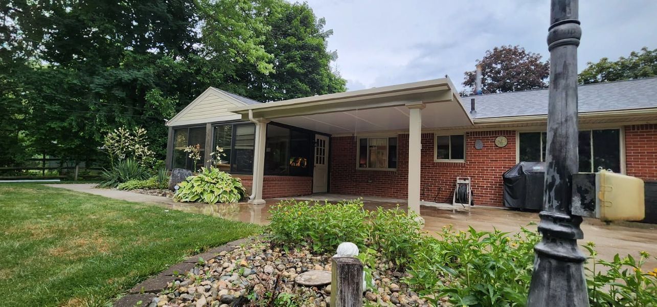 Brick house with a covered patio, screen room, and lush landscaping. Overcast sky.