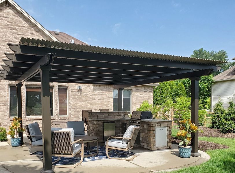 Pergola with outdoor kitchen, seating area, and brick house in the background.