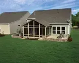 A gray house with a screened-in porch and patio on a grassy lawn.