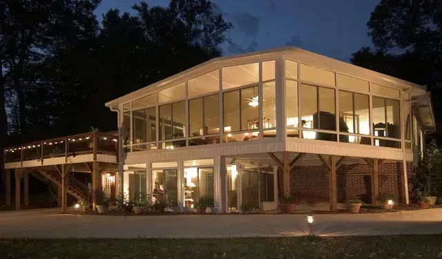 Two-story modern home with large glass windows illuminated at night, surrounded by trees.
