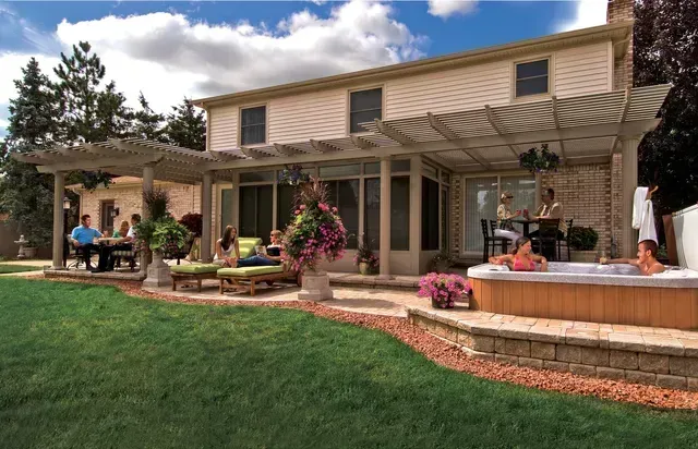 Two-story home with patio, pergola, and hot tub. People relax and socialize on the patio and in the hot tub.