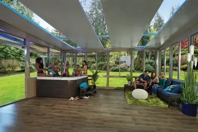 People relax in a sunroom with a hot tub and seating, overlooking a backyard.