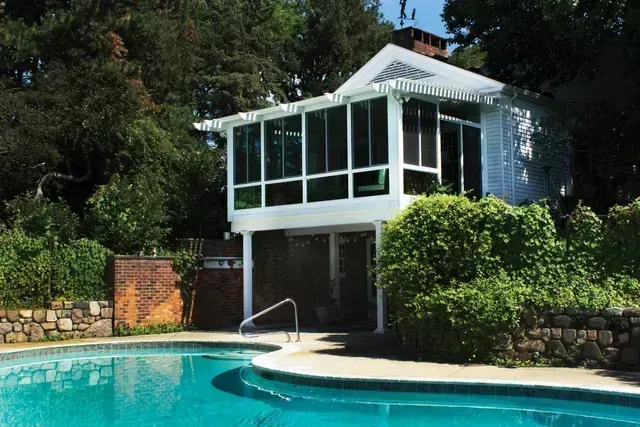 Poolside building with a screened-in porch. The porch is white and the water in the pool is blue.