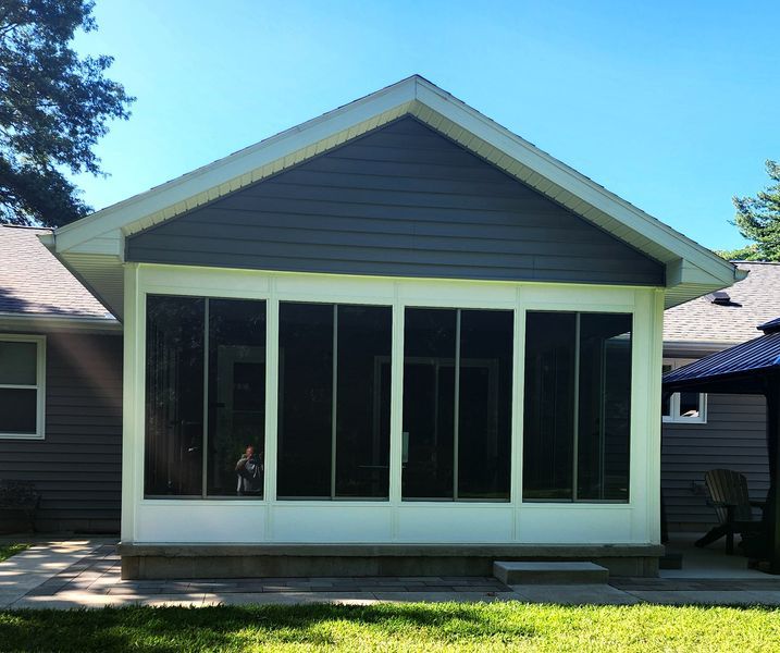 Screened-in porch addition with white framing, dark blue siding, and a person visible inside; viewed from a grassy yard.