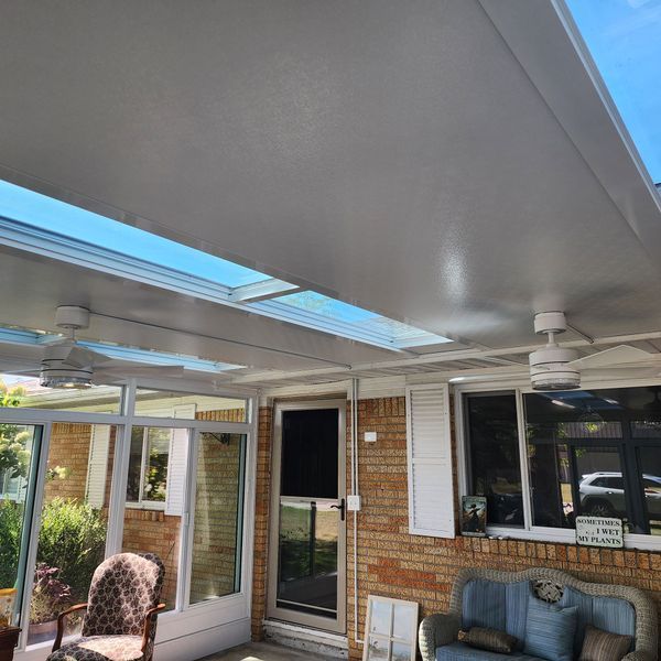 Covered patio with skylights, ceiling fans, and brick wall.