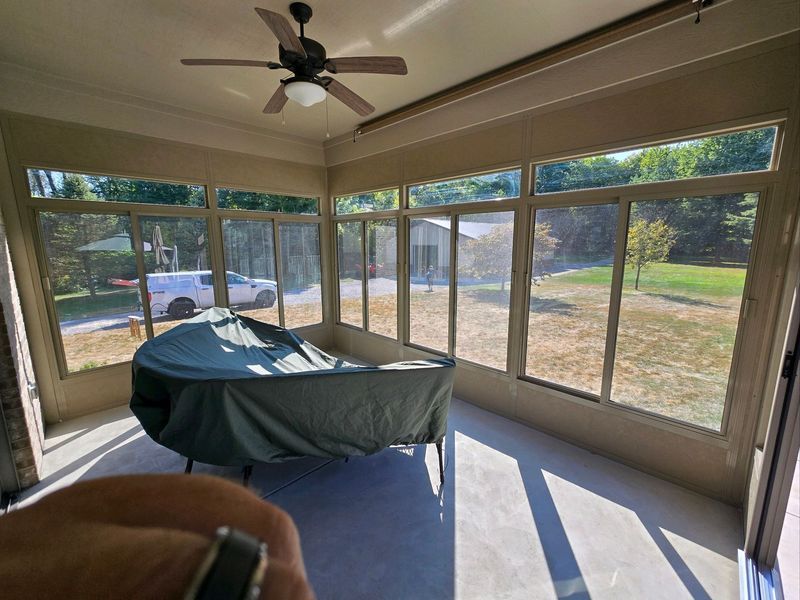 Sunroom with large windows, covered table, ceiling fan, and view of a yard.