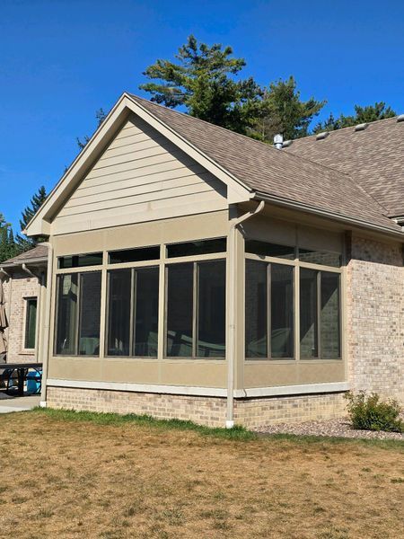 Tan screened-in porch with multiple windows attached to a brick home on a sunny day.