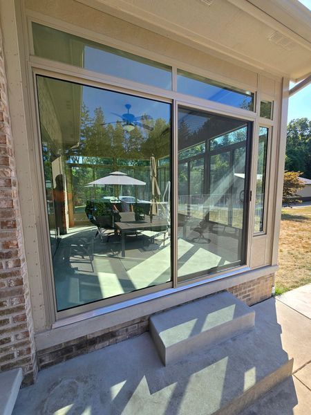 Large glass sliding door and window overlooking a patio with a table, chairs, and umbrella.