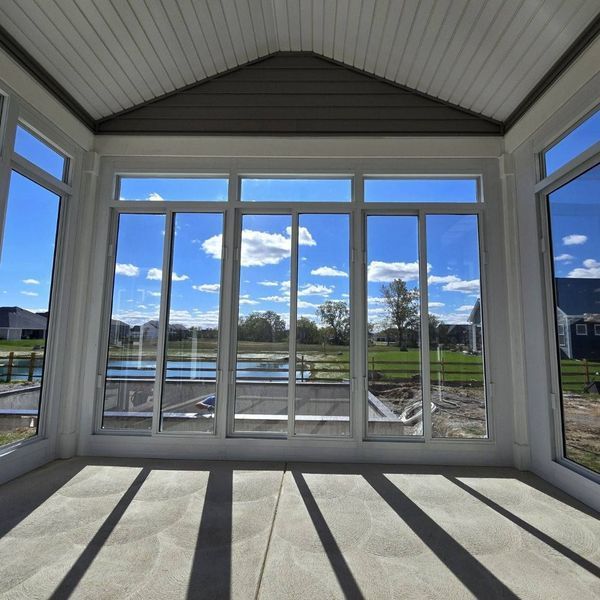 Sunroom with large windows, bright sky view, shadows cast on floor.