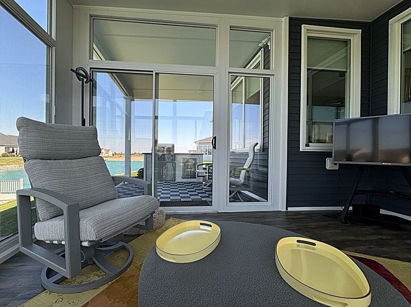 Sunroom with a gray rocking chair, round table with trays, and sliding glass doors overlooking a lake.