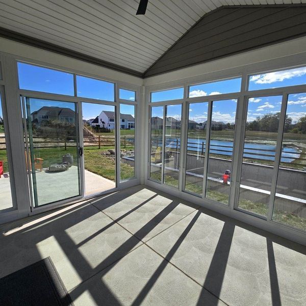 Sunroom with large windows overlooking a backyard and pond on a sunny day.