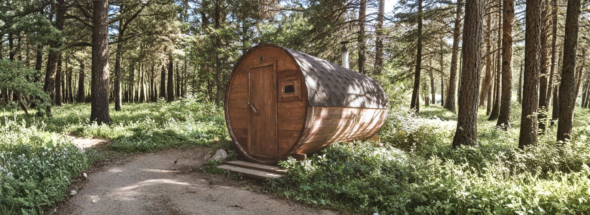 Barrel-shaped wooden cabin in a forest clearing, dirt path leading to the entrance.