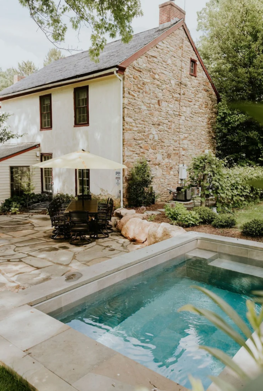 Backyard with a stone house, pool, patio, and dog sunbathing.