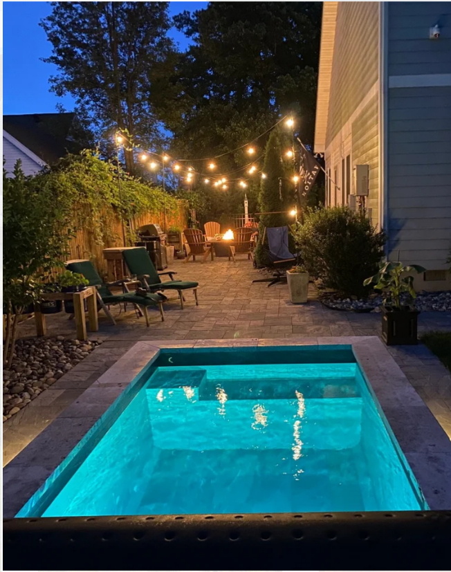 Backyard with illuminated pool, string lights, and fire pit at dusk.