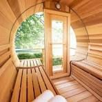Inside a cedar barrel sauna, benches, towels, glass door, and exterior view.