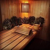 Wooden sauna interior with benches, plants, and a small wooden bucket.
