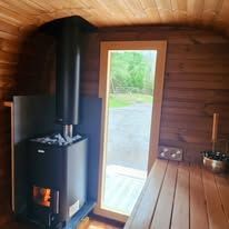 A wooden sauna interior with a wood-burning stove and a glass door.