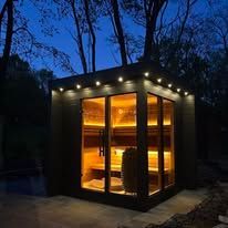 A sauna illuminated at night; wooden structure with lights and glass windows set among trees.