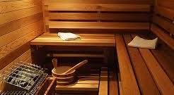 Wooden sauna interior with benches, heater, bucket, and towel.