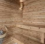 Wooden sauna interior with benches, stones in a bucket, and warm lighting.
