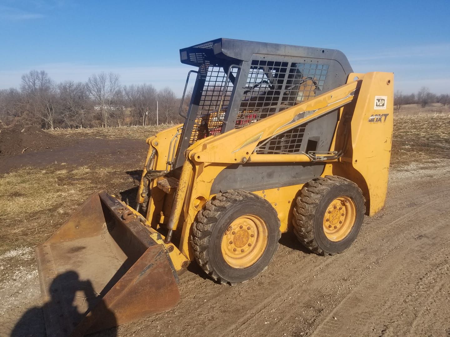 A yellow skid steer is parked on a dirt road