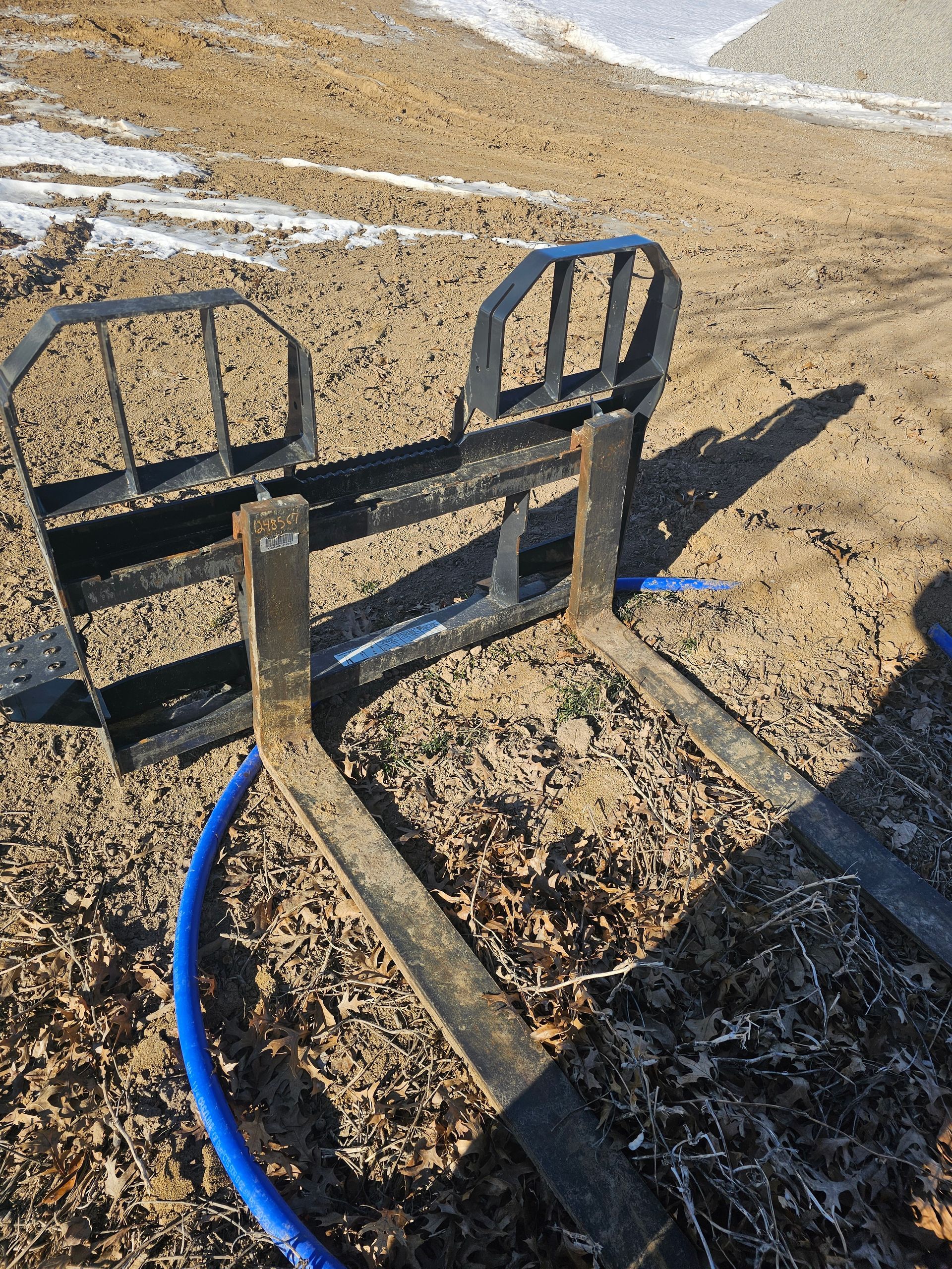 A pair of forks sitting on top of a dirt field next to a blue hose.