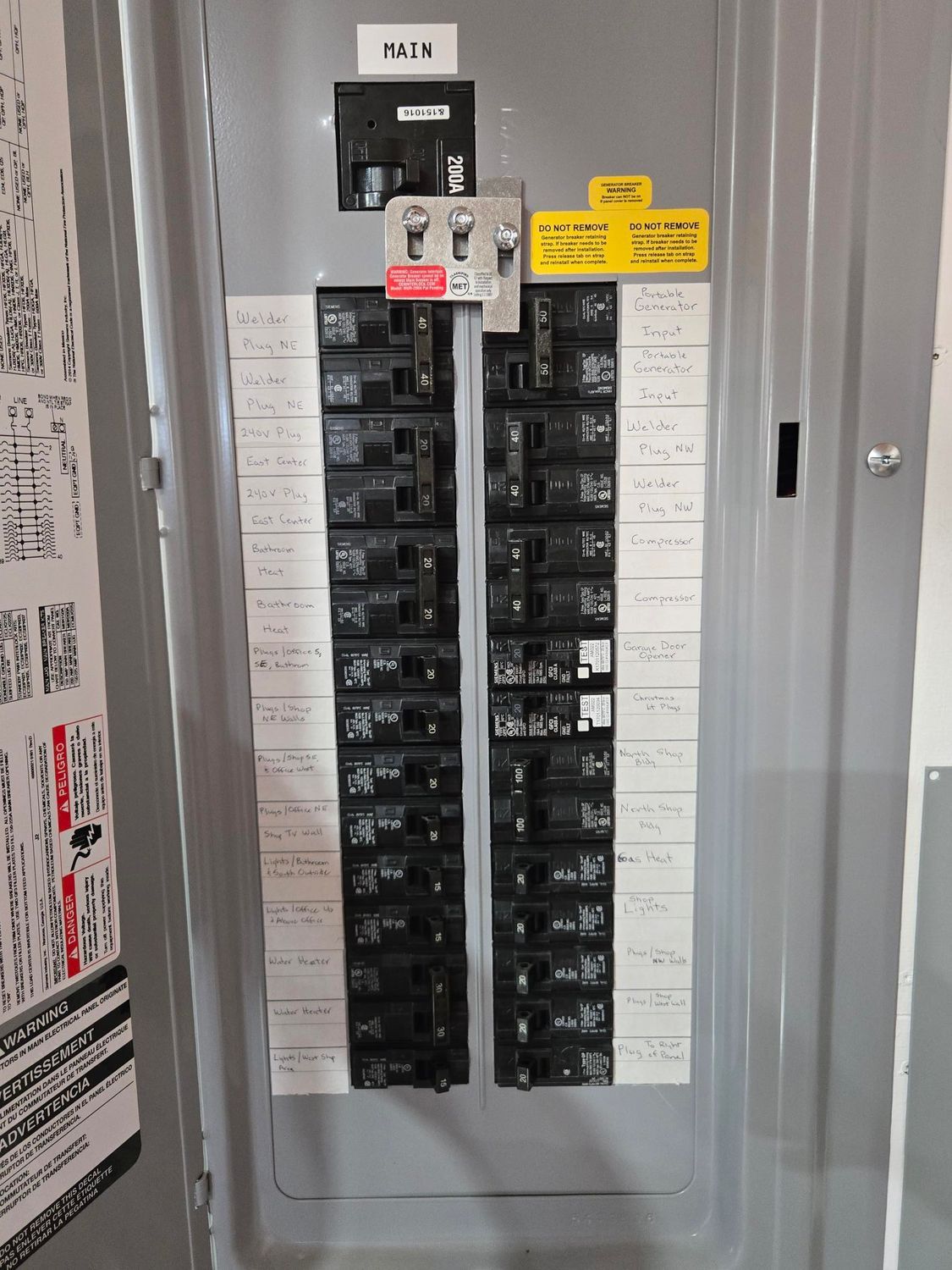 Electrical breaker panel with rows of black circuit breakers and a yellow warning label inside a gray cabinet.