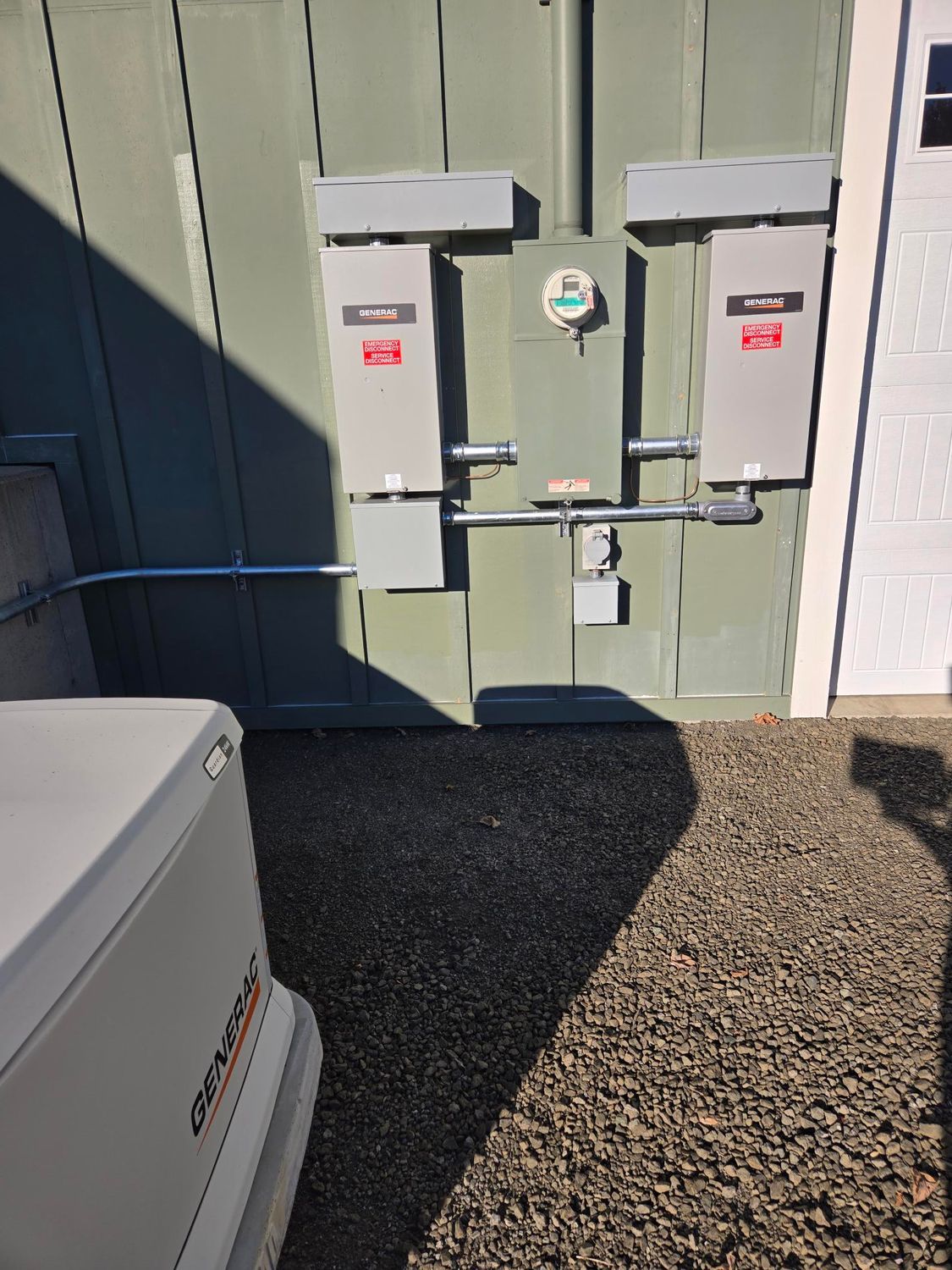 Electrical meter boxes mounted on a gray exterior wall beside a white door and gravel ground