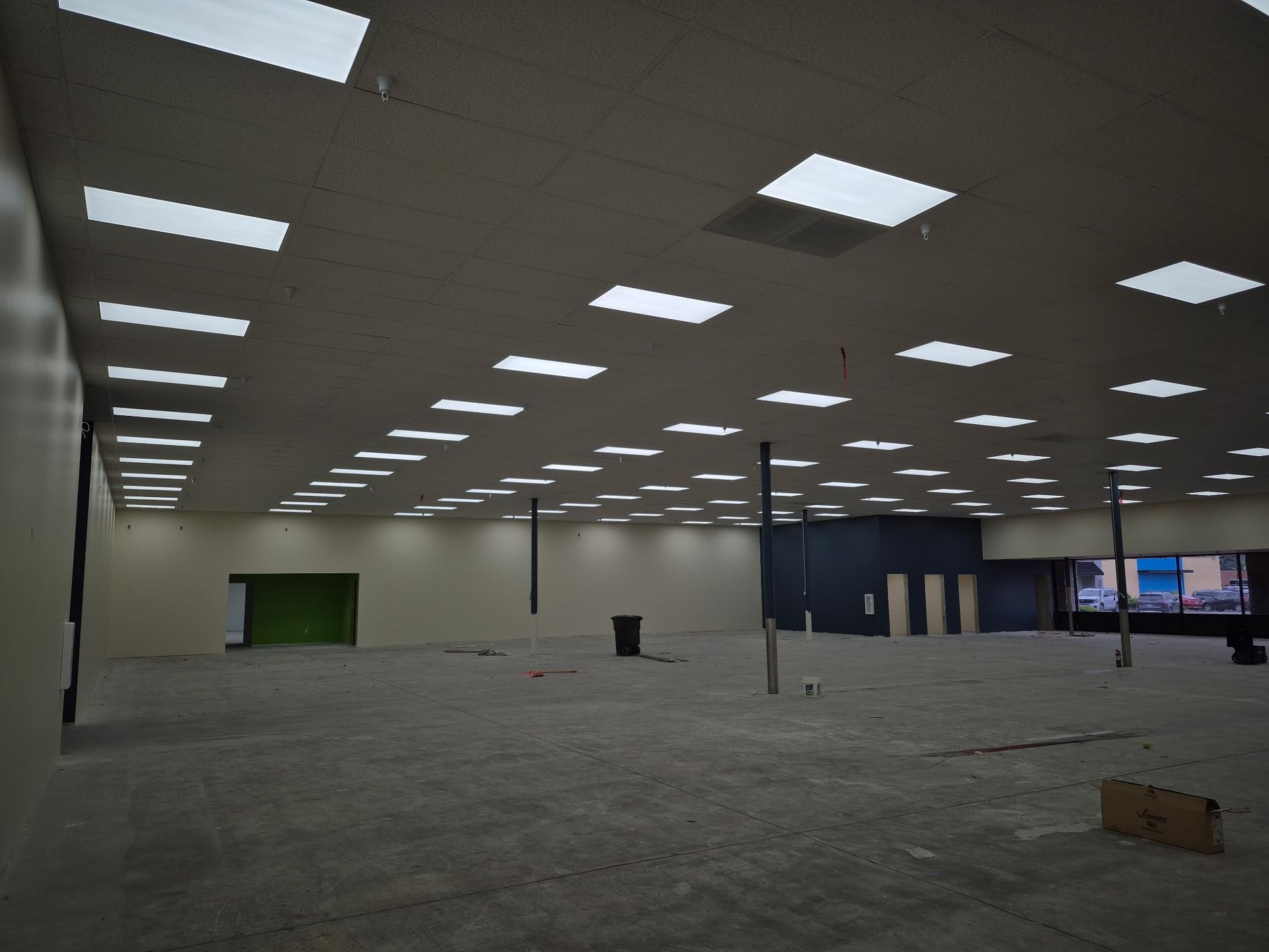 Empty unfinished warehouse with gray floor, white ceiling lights, and a few columns and openings.