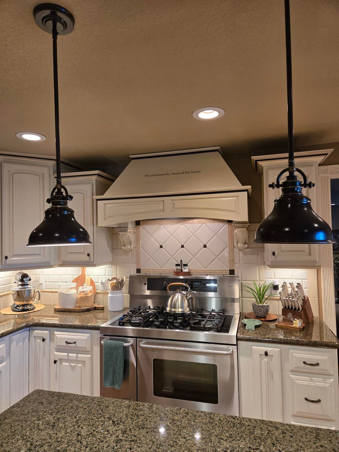 Modern kitchen with white cabinets, black pendant lights, granite island, and stainless steel stove under a hood
