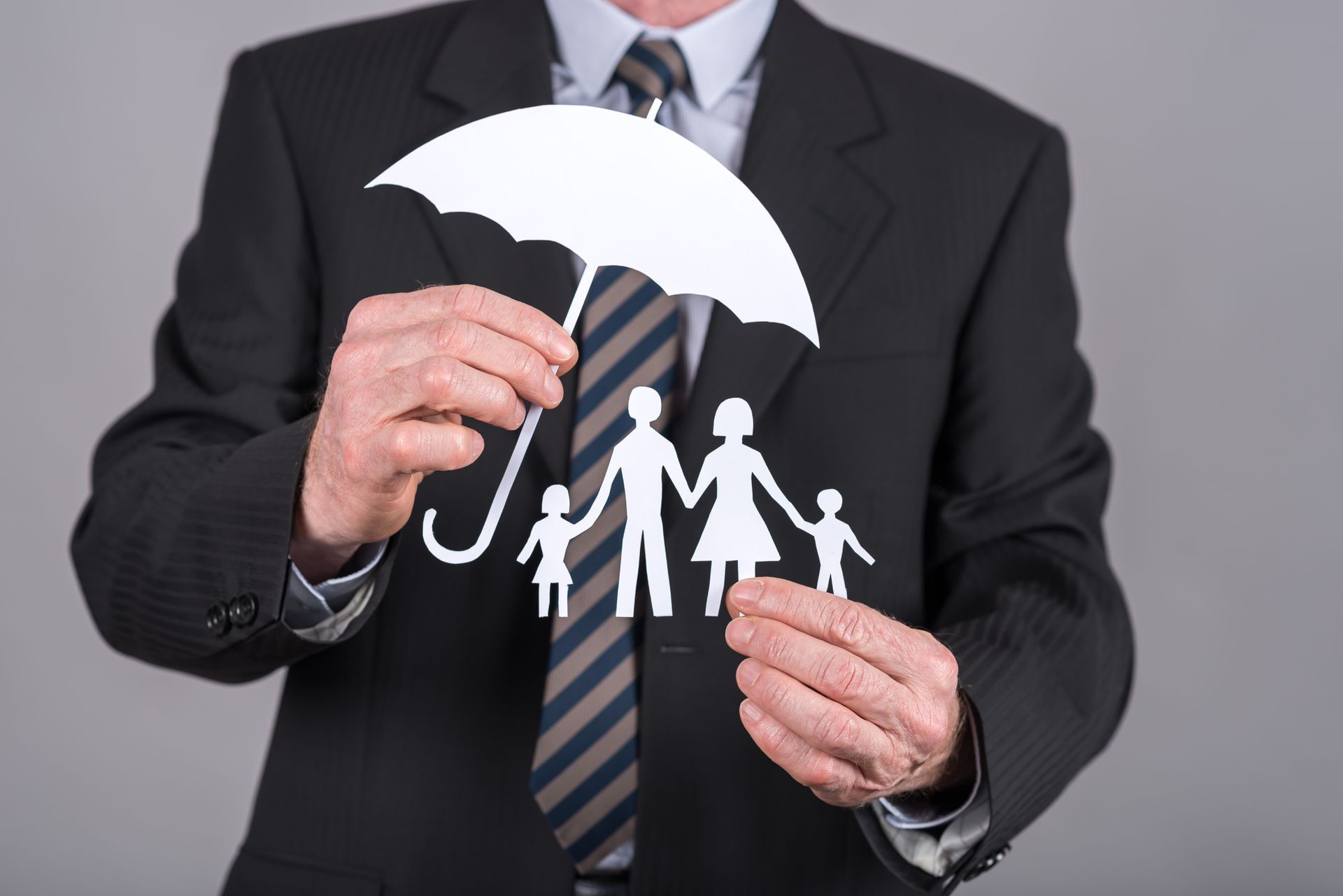 Man in suit holding a paper cut-out of a family under an umbrella.