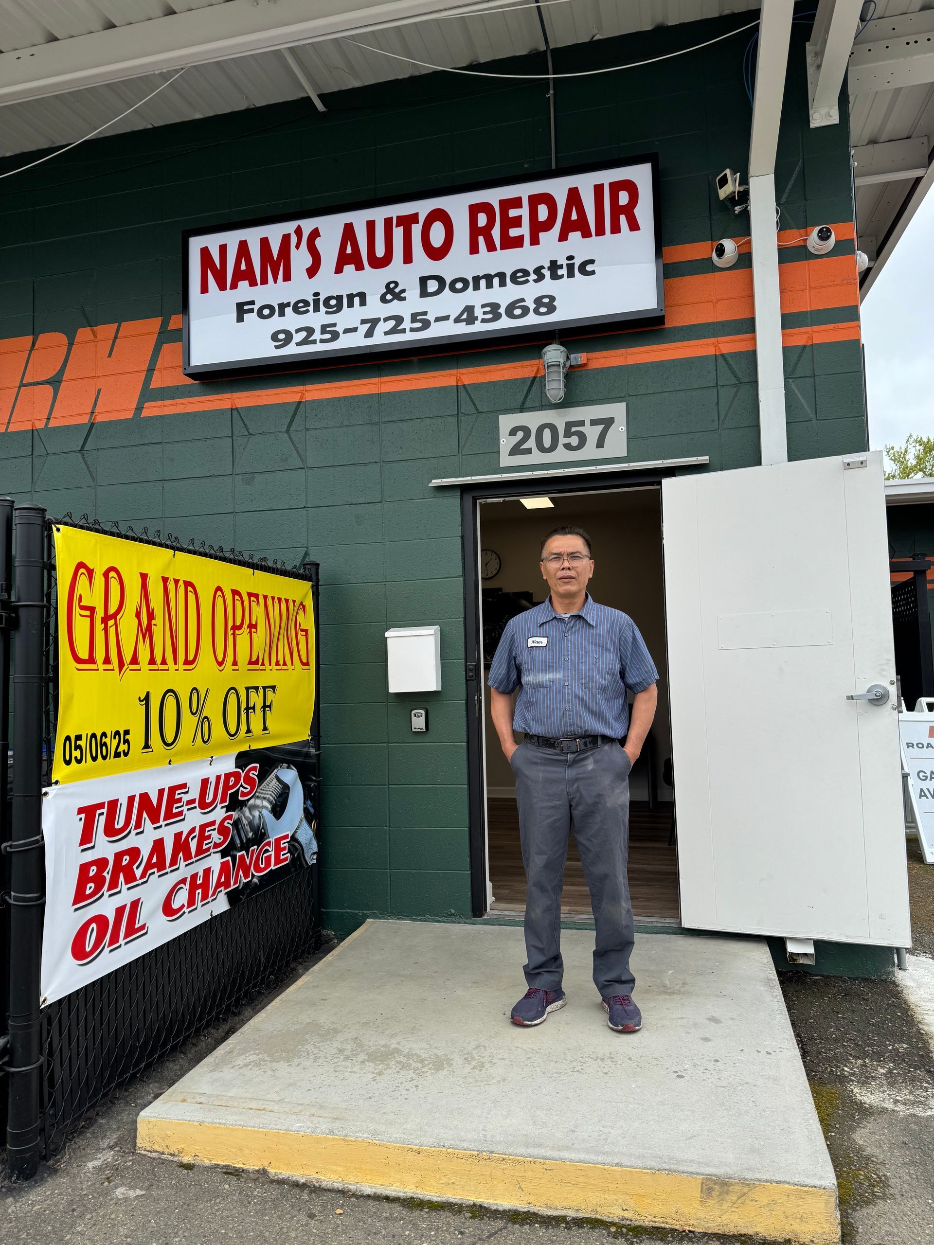 A man is standing in front of a car repair shop.