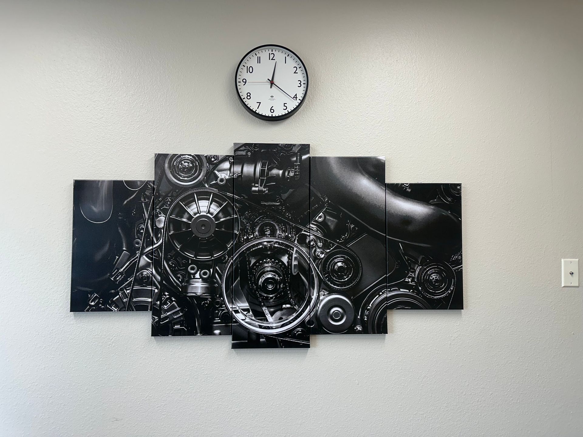 A clock is hanging on a wall next to a painting of a engine.