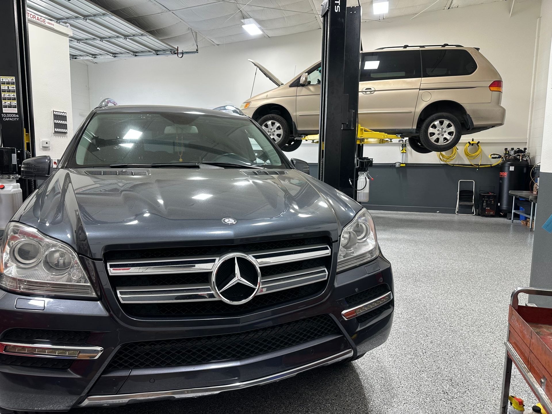 A mercedes benz is parked in a garage next to a van on a lift.