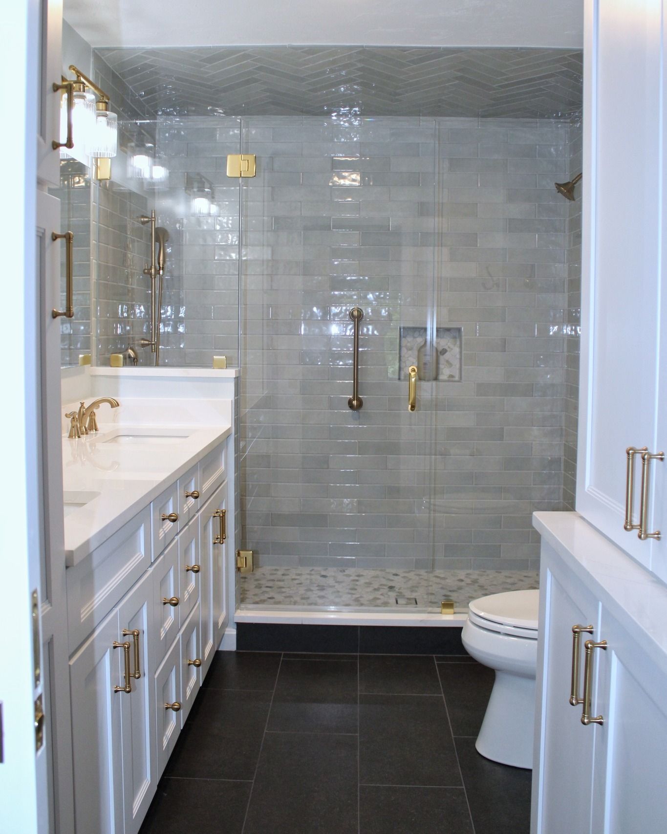 Bathroom with white cabinets, gold fixtures, gray tile shower, black floor, and a toilet.