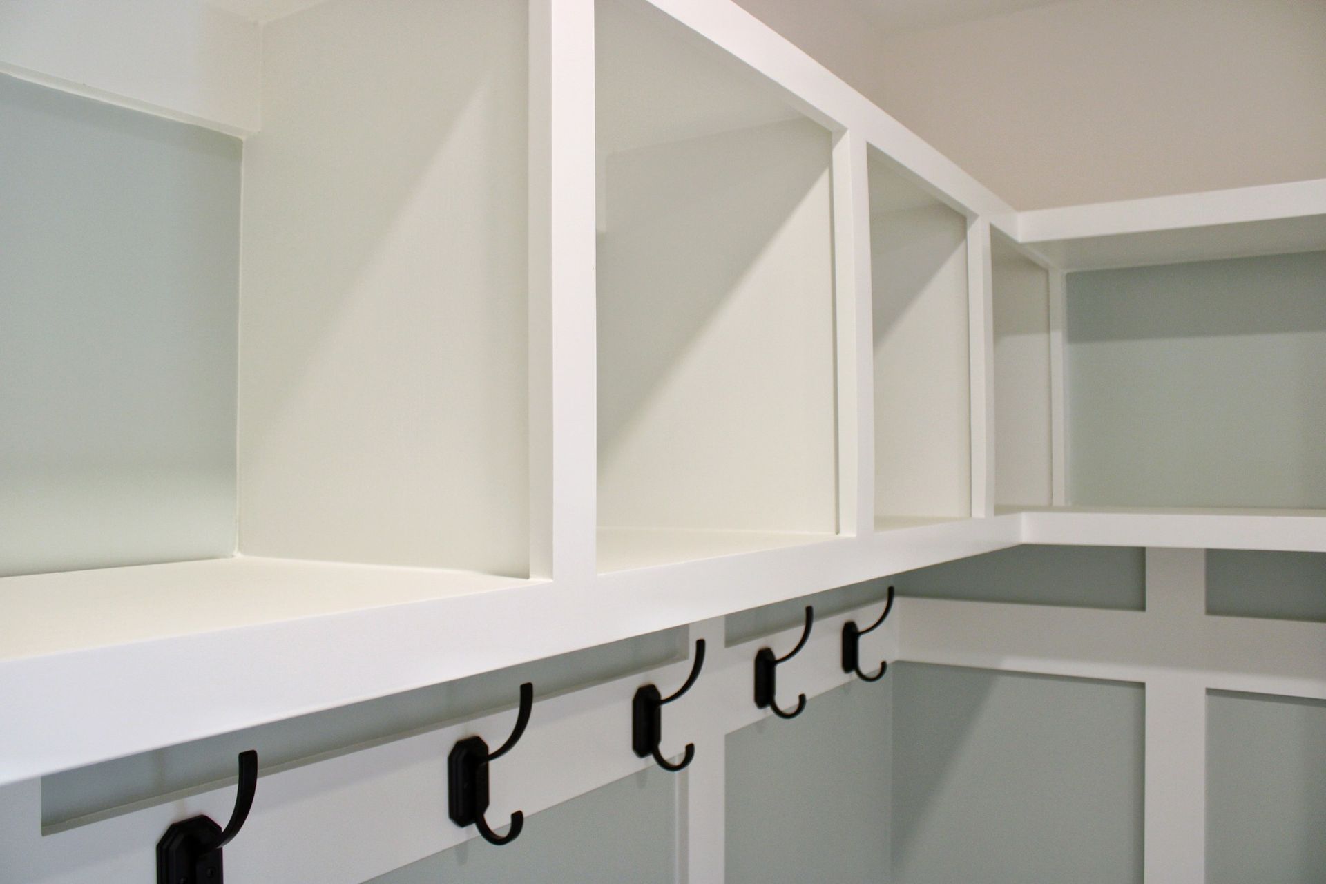 White built-in storage unit with open shelves and coat hooks in a light blue room.