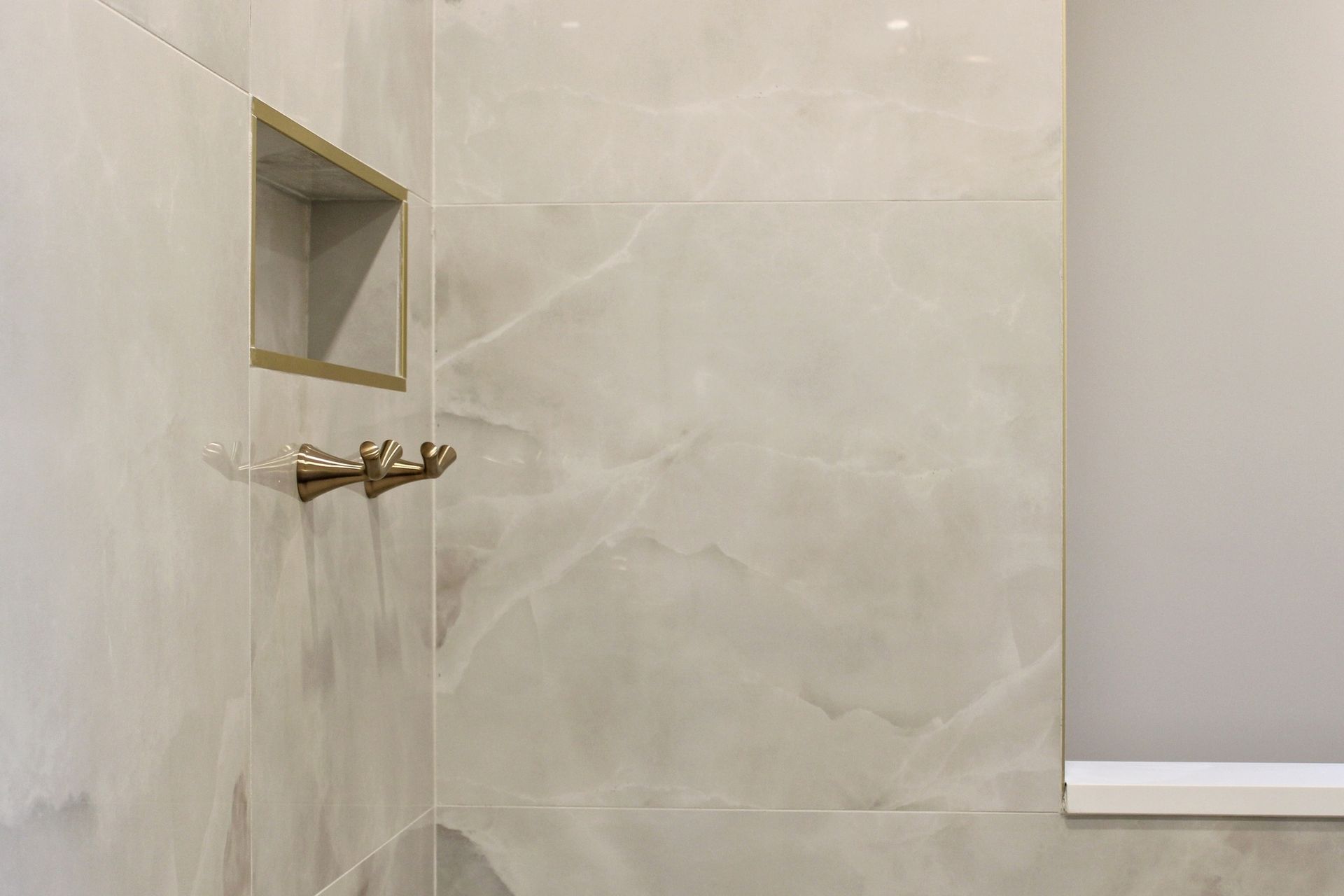 Shower interior with light-colored marble-like tiles, a built-in shelf, and gold-colored fixtures.