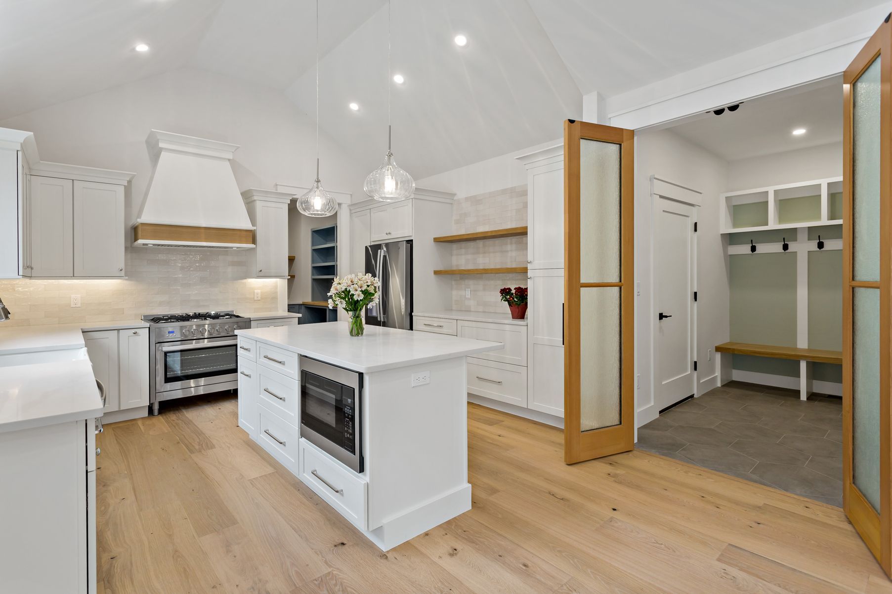 White kitchen with island, stainless steel appliances, light wood floors, and open doorway to a mudroom.