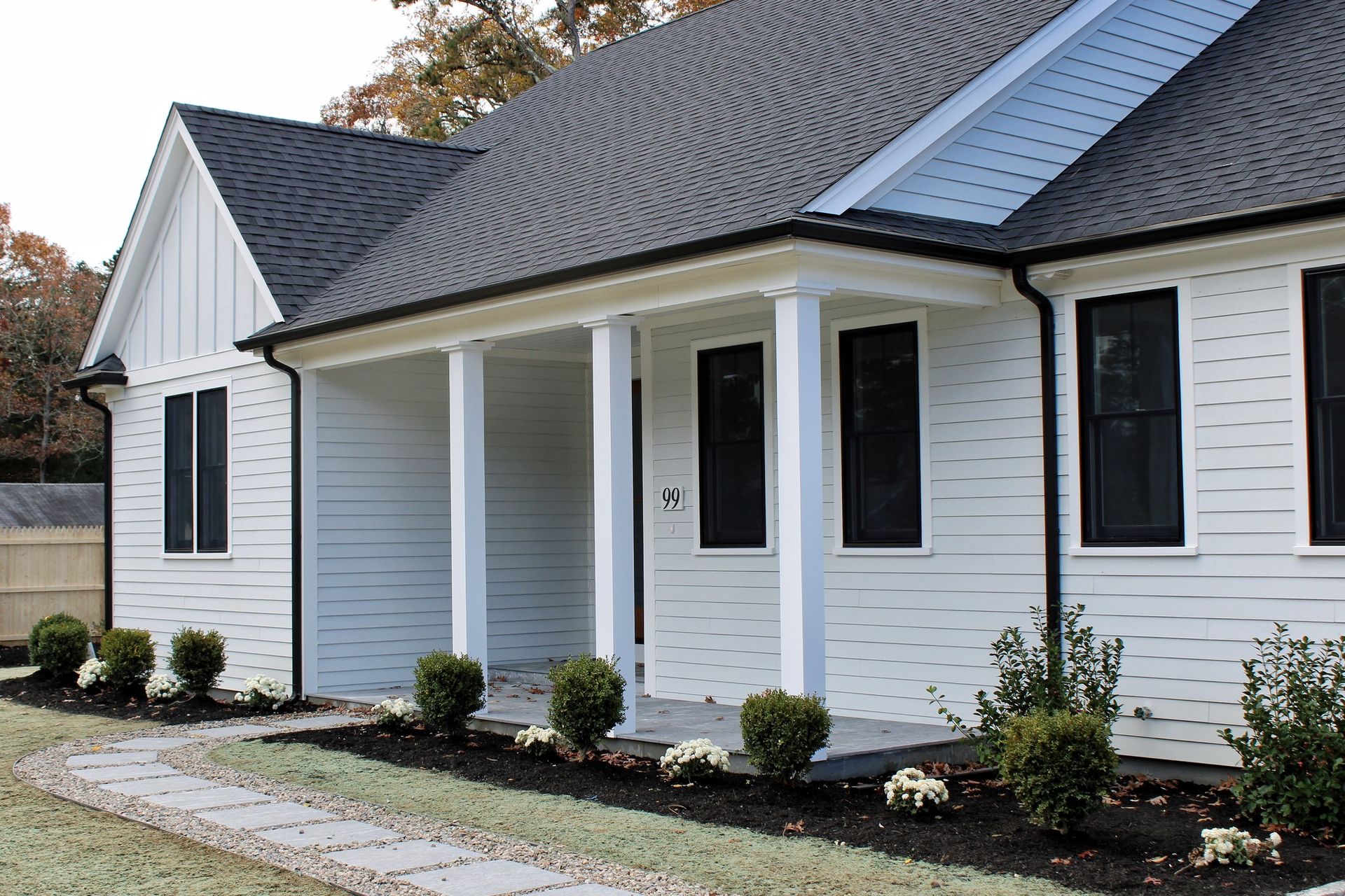 White house with black windows and roof, porch with pillars.