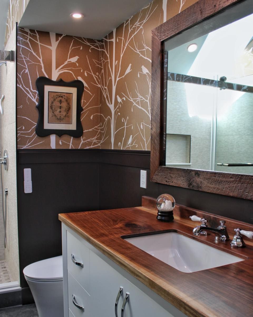 Bathroom with wood countertop, white sink, patterned wallpaper, and framed mirror.