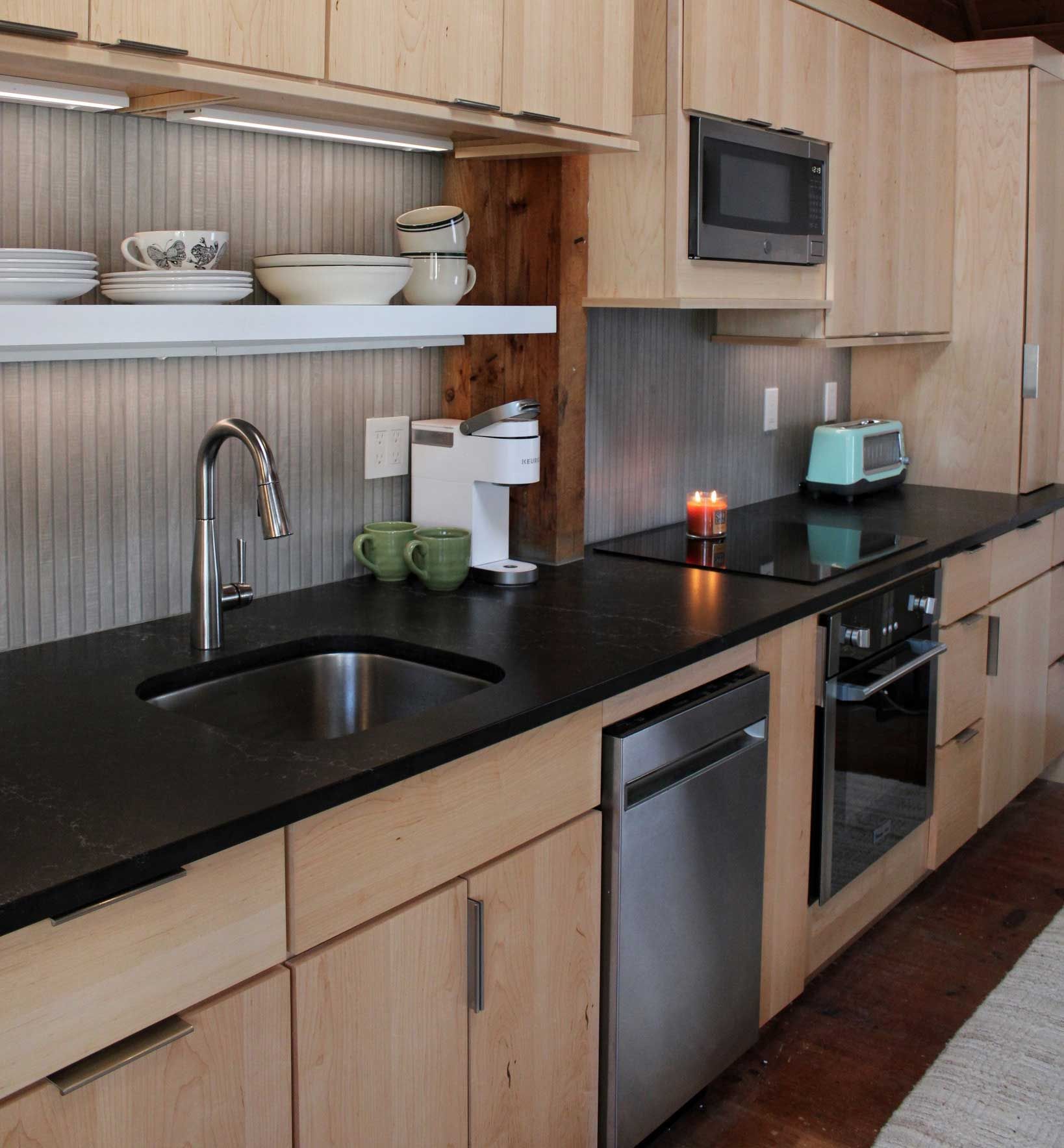 Kitchen with light wood cabinets, black countertop, stainless steel appliances, and a built-in oven.