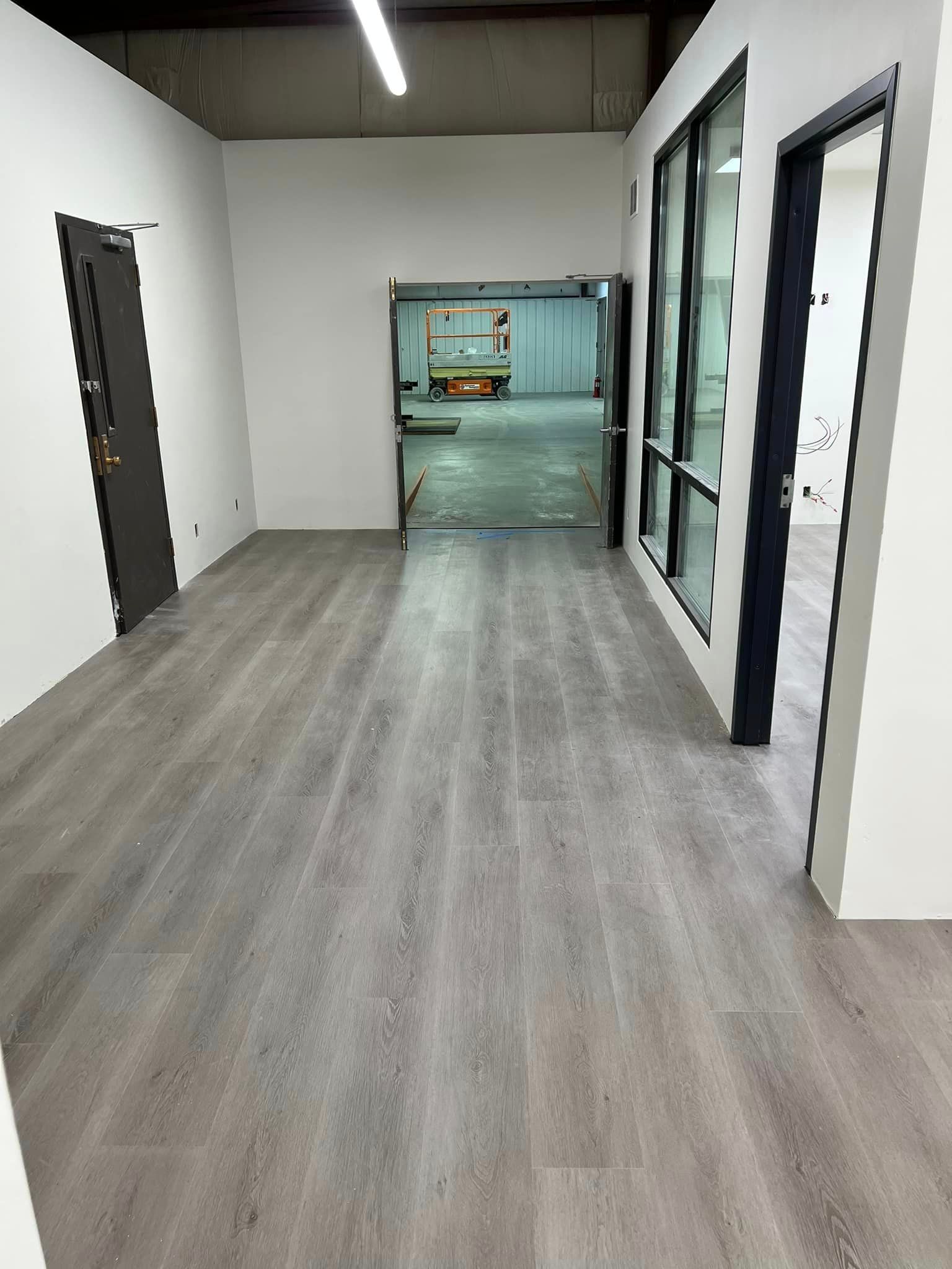 A long hallway with a wooden floor and white walls leading to a warehouse.